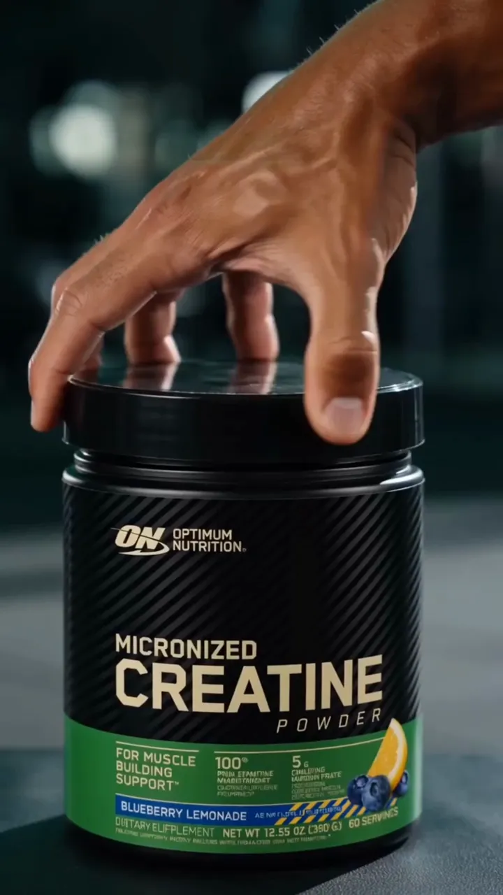 A hand reaching for an Optimum Nutrition creatine container in a dark gym setting